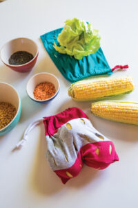 red and gray produce bag with fruit in it sitting on a table with corn…